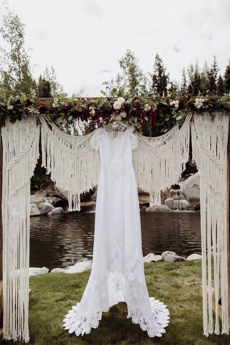A wedding gown hanging from a macramé arch beside the pond