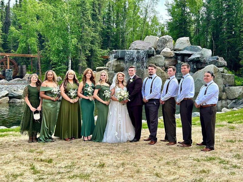 A bridal party in sage green standing in front of the waterfall