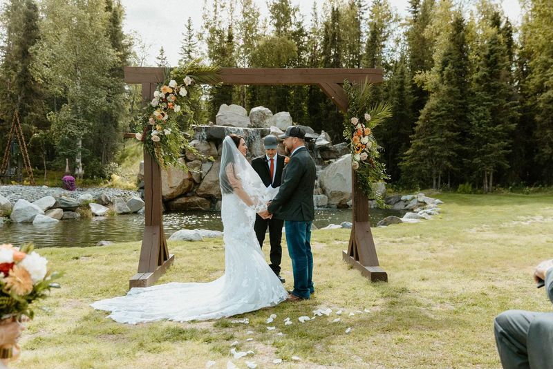 A couple exchanging vows under a wooden floral arch