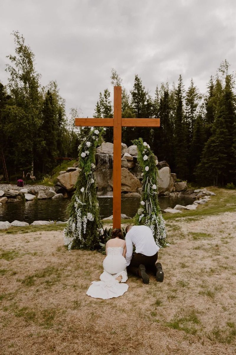 A newly married couple kneeling at the wooden cross in front of the waterfall