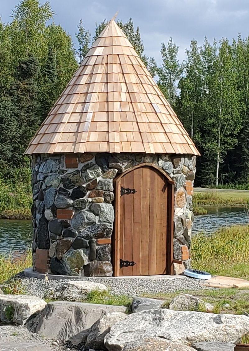 A stone cottage with a cedar-shingle roof beside the pond