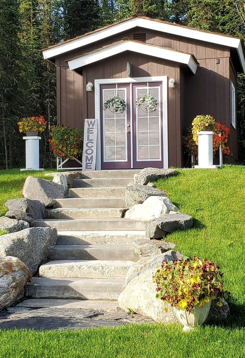 The she-shed with its welcome sign, flowers and stone steps