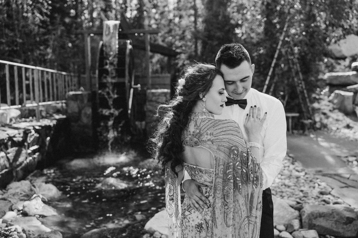 Black-and-white photo of a couple embracing by the waterwheel creek